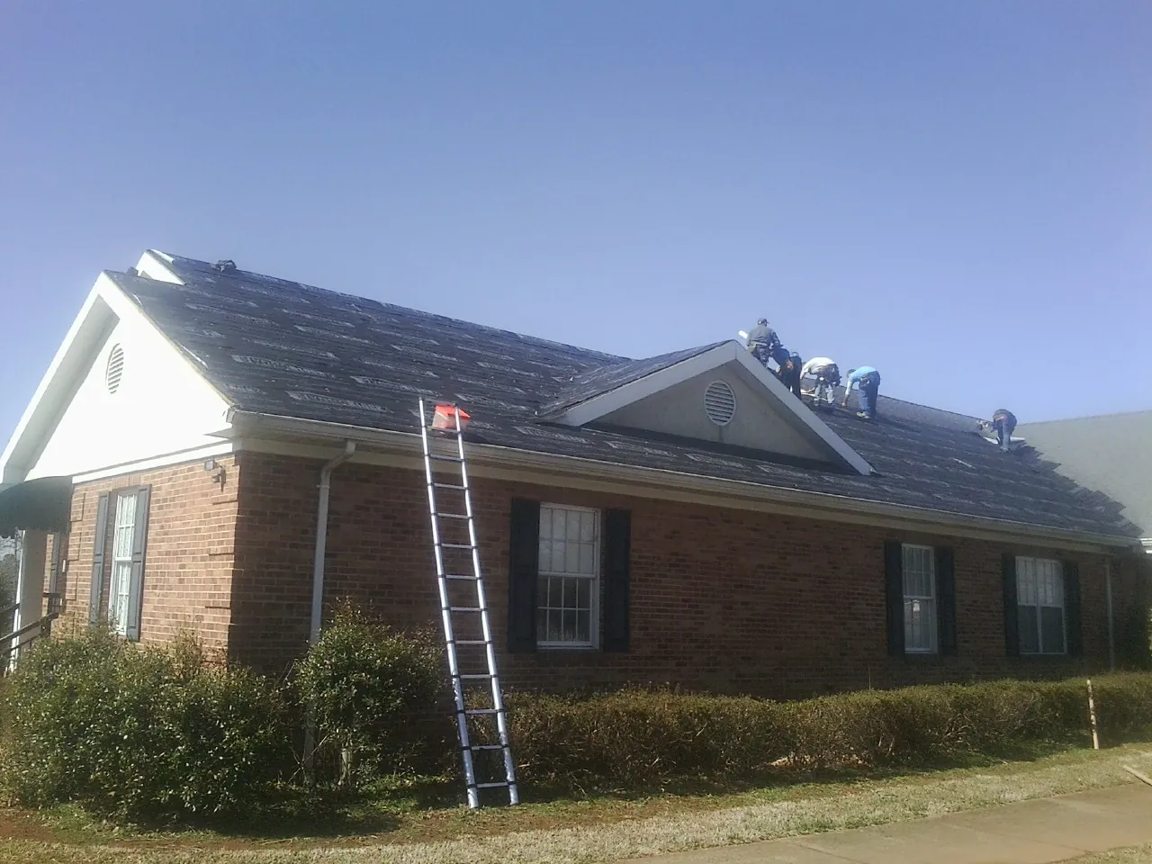 Crew tearing shingles off a brick ranch roof with a ladder set — Emergency Roof Repair work by our crew in Council