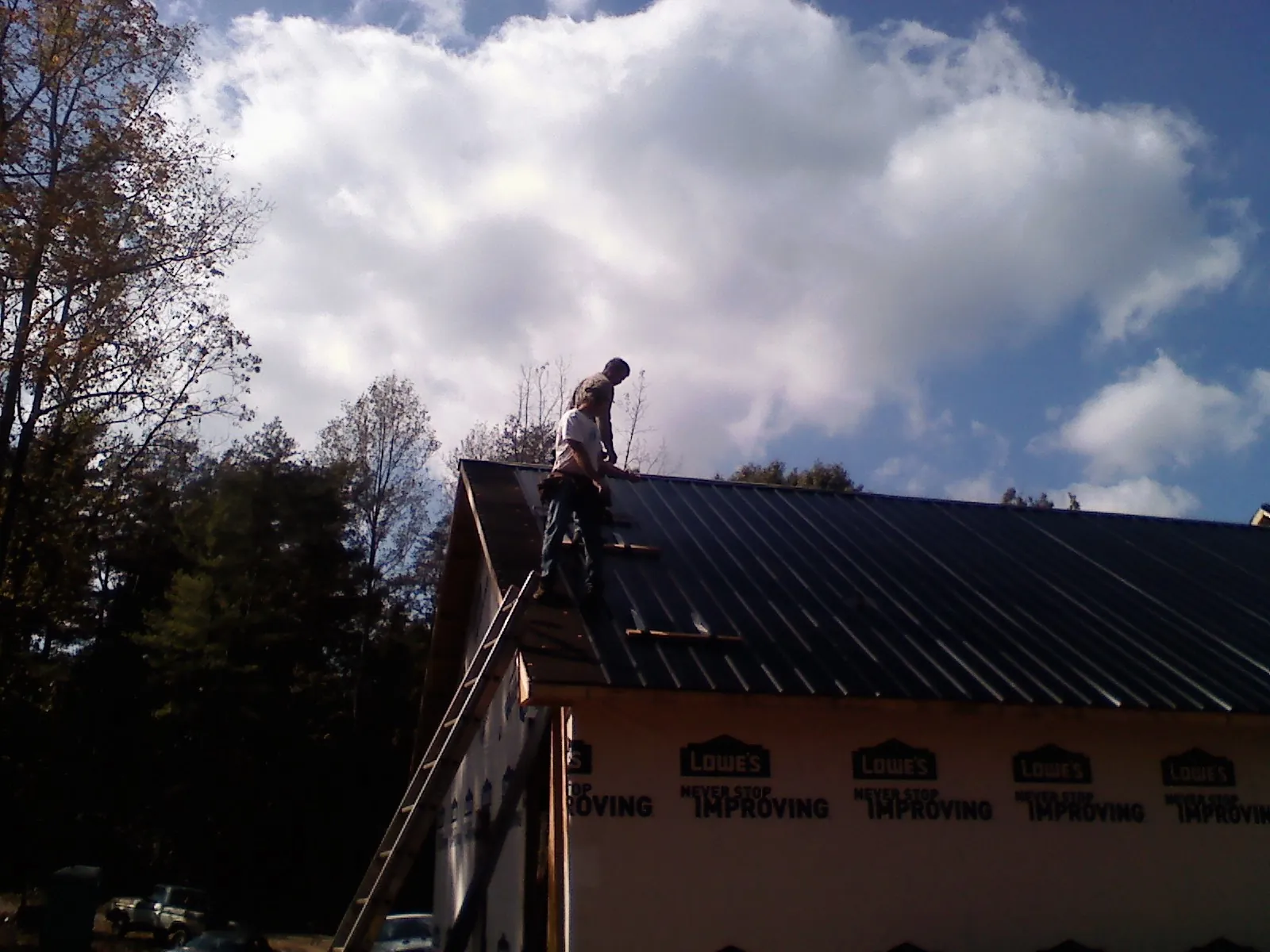 Roofer fastening dark metal panels high against a cloudy sky, from a Roof Inspection job in Council