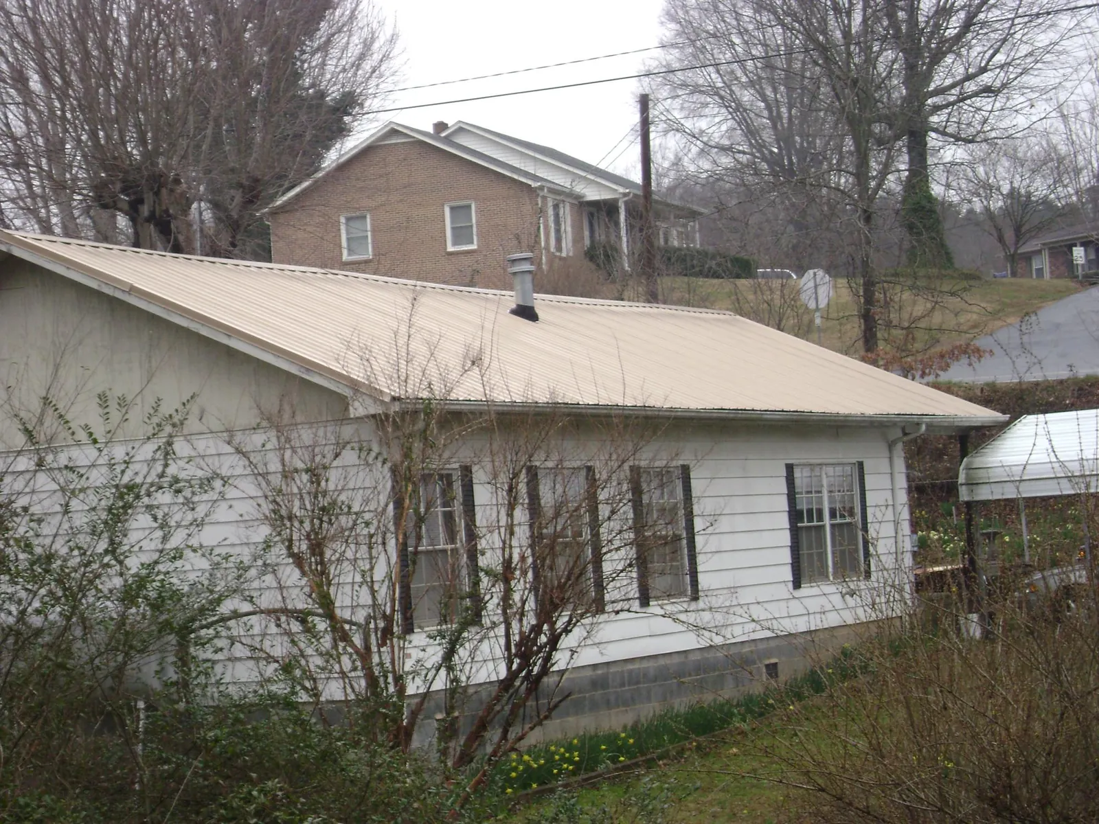 Tan metal roof on a white sided house set into a hillside — Commercial Roofing by Roofing Brothers in Council
